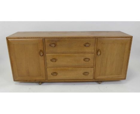 An Ercol blond elm Windsor sideboard, having three central drawers flanked by conforming cupboard doors on roller castors, h.