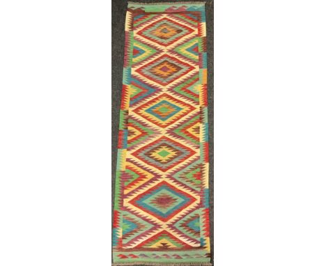 A Turkish Anatolian Kilim runner carpet, knotted with a central row of five diamond-shaped medallions, in bright colours, red