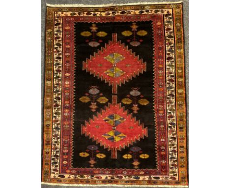 A North west Persian Heriz rug / carpet, hand-knotted in dark tones of red, blue, and green, on a black ground, the central f