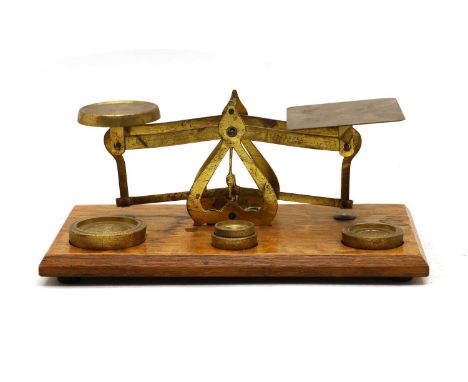 An Edwardian gilt brass postal scale, with four weights on an oak base, 20.5cm wide, together with a larger example, the lett