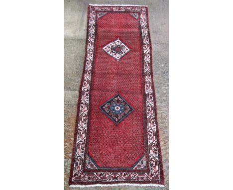 A Persian Hamadan hand knotted woollen runner with two central diamond motifs within a stylised border on a beige ground, 286