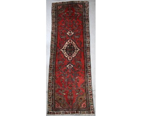 A Persian Hamadan hand knotted woollen runner with central motif within a stylised border on a red ground, 310 by 95cms (122 
