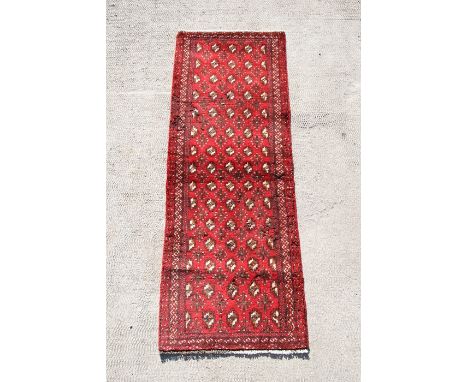 A Persian Balouch woollen hand knotted runner with repeat design on a red ground, 193 by 67cms (76 by 26.5ins).