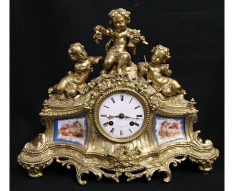 Marshall & Fils of Paris. Victorian gilded brass mantle clock surmounted with three cherubs, inset Serves style porcelain pan