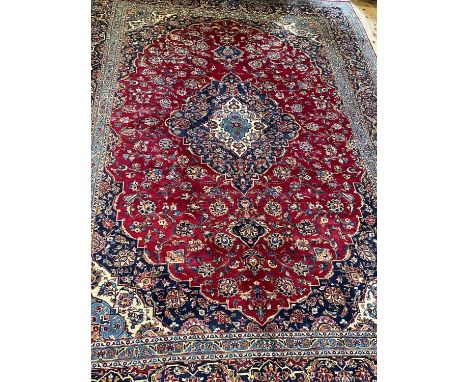 A KASHAN CARPET, the crimson floral field centred by an ivory and blue gul, similar spandrels within an indigo foliate main b