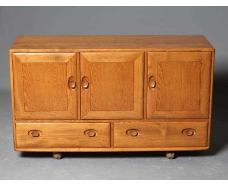 AN ERCOL WINDSOR MODEL 468 SIDEBOARD, in blond elm, the fascia with three blind panel cupboard doors enclosing shelving over 