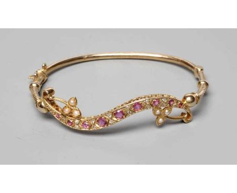 AN EDWARDIAN STYLE STIFF HINGED BANGLE, the scrolling upper section pave set with graduated facet cut rubies with pairs of di