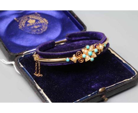AN EDWARDIAN STIFF HINGED BANGLE, the upper section centred by a turquoise bead and seed pearl flowerhead flanked by wirework