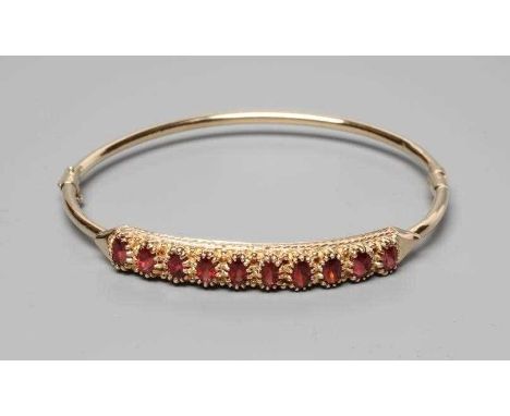 A STIFF HINGED BANGLE, the upper section claw set with ten oval facet cut garnets, indistinctly stamped (Est. plus 24% premiu