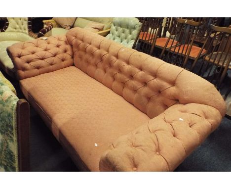 A Victorian three seater button-back Chesterfield sofa having salmon pink upholstery resting on turned supports and brass cas