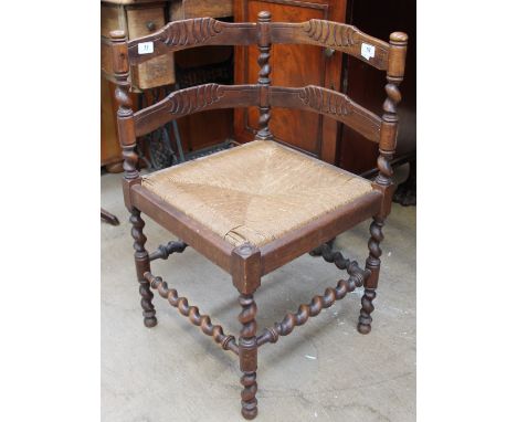 An early 20th century corner chair with ladder backs above a rush seat on turned legs united by stretchers