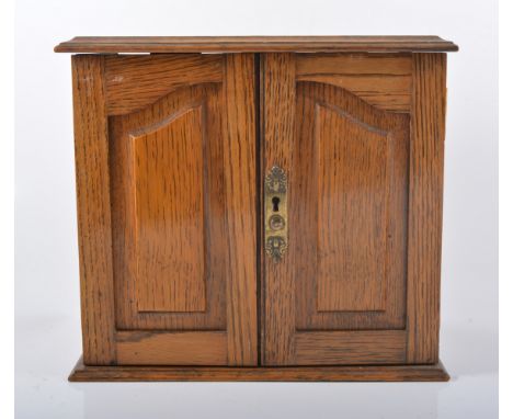 Oak table top tobacco cabinet, hinged top concealing pipe rack above a pair of panel doors,  W25cm, H25cm.