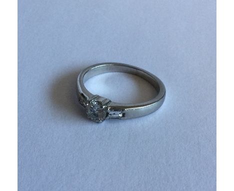 An attractive diamond single stone ring in claw mount with baguette cut shoulders. Approx. 3 grams. Est. £100 - £200.