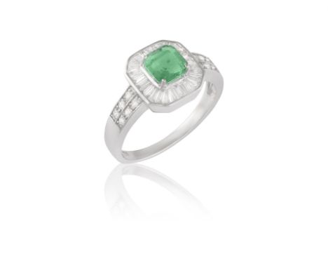 An Emerald and diamond cluster ringThe rectangular cut-cornered emerald, bordered by tapered baguette-cut diamonds, to brilli