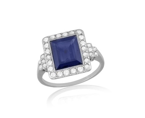 A Sapphire and diamond cluster ringThe rectangular step-cut sapphire in a millegrain setting, bordered by single-cut diamonds