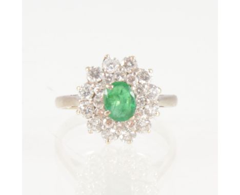 An emerald and diamond oval cluster ring, the oval mixed cut emerald 6.5mm x 5mm, claw set and surrounded by two rows of bril