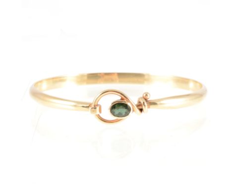 Tom Payne - A 9 carat yellow gold tension style bangle set with tourmaline, the oval mixed cut green tourmaline collet set in