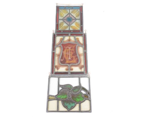 Three Victorian stained glass panels, one with monogrammed shield, enclosed by ruby border, 28cm x 22.5cm; the second with ce