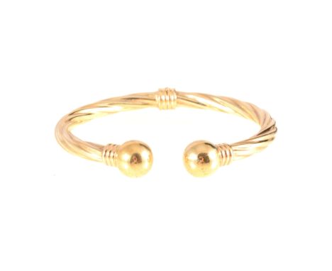 A 9 carat yellow gold torque bangle, 5.8mm wide hollow twisted design with a 12mm bead to each end and hinged at the back, ap