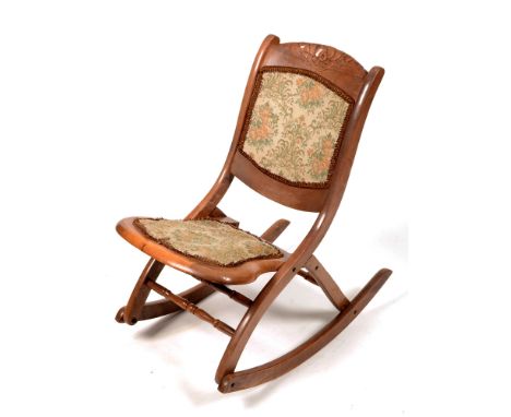 An early 20th Century walnut framed folding rocking chair, the curved top rail with a carved rosette above a padded back and 