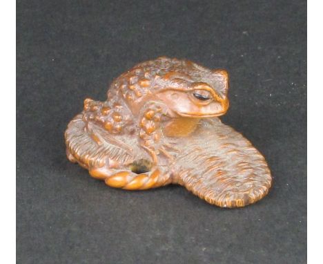 A small Japanese wood Netsuke of a Toad by Masanao, Meiji Period, Seated on an upturned waraji (straw sandal), its body twist
