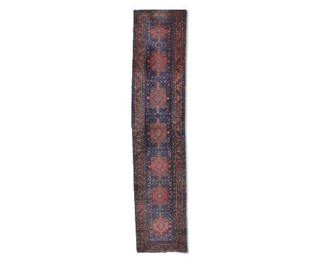 A NORTH WEST PERSIAN RUNNER. 428 X 92CMthe oblong centre field woven with seven geometric medallions, in ochre against a navy