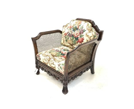 Early 20th century polished beech carved bergere armchair, shaped cresting rail and out swept arms over scrolling moulded dec