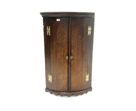 18th century George III oak bow front wall hanging corner cupboard, projecting cornice over two mahogany cross banded doors e