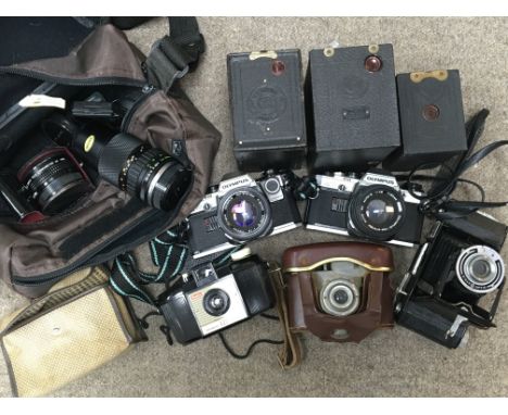 A box containing a collection of cameras including two Olympus OM10s, an Olympus 75-150mm lens, Kodak box brownies, and a Ita