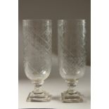 A PAIR OF GLASS STORM LANTERNS on square stepped bases. 34cms high.