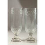 A PAIR OF GLASS STORM LANTERNS on square stepped bases. 34cms high.