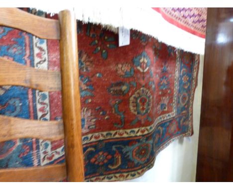 An early 20th Century Middle Eastern wool floor rug, decorated with central panel of flowers on a red background surrounded b