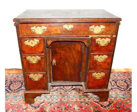 A Georgian walnut kneehole desk, having an arrangement of seven drawers with brass handles, and a cupboard door to the recess