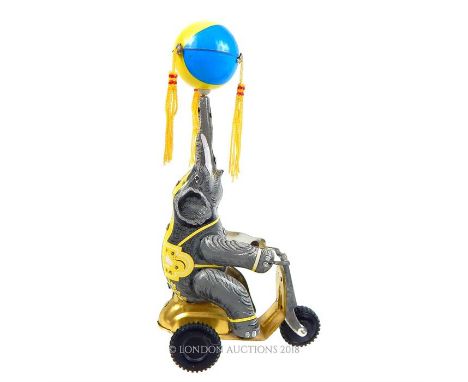 A tin plate, wind-up toy in the form of an elephant on a cycle and balancing a beach ball on trunk, Height: 16 cm, Width: 14 