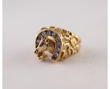 RUBY AND DIAMOND RING. As a horse's head, with ruby set eye, to a diamond set horseshoe, to textured shoulders, stamped '18K'