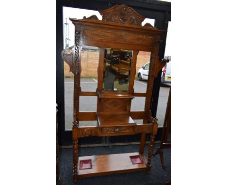 A late Victorian oak hall stand, shaped pediment centred by a Green Man mask above a bevelled mirror plate and walking stick/