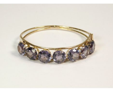 GOLD BANGLE. A 14ct. gold hinged bangle, the front set with seven faceted synthetic colour-change sapphires. Approx. 17.1g.  