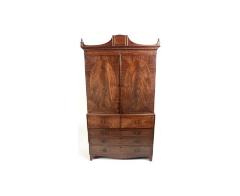 A George III mahogany secretaire press, with shaped cornice and inlaid frieze above a pair of doors with oval veneered panels