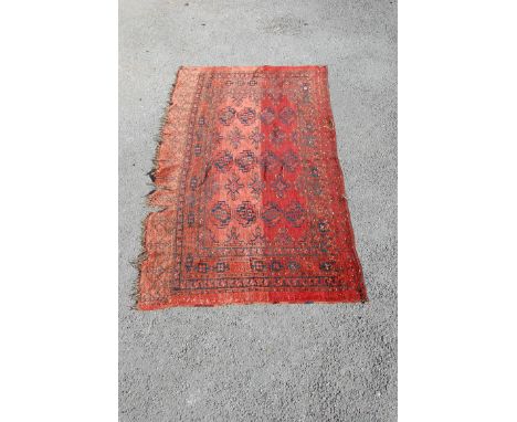 A large scale antique Tekke torber hand woven floor rug having a red ground with black borders and repeating medallions to th