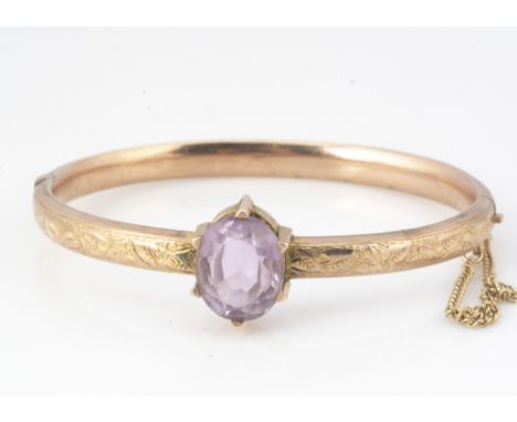 A Victorian 9ct gold and amethyst hinged bangle, the central mixed oval amethyst in six claw setting with an engraved surroun