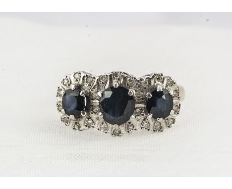 A three stone sapphire and diamond 18ct gold dress ring, the three circular claw set sapphires within a diamond set tablet in