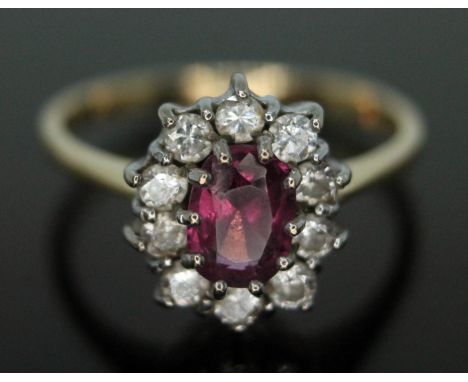 A cluster ring set with a central oval cut pinkish purple almandine garnet and surrounded by ten round brilliant cut diamonds