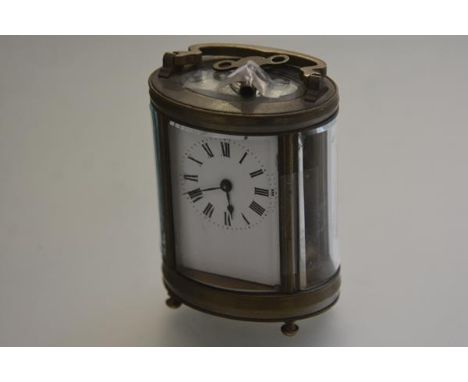 An Edwardian French oval brass four glass carriage clock with brass handle to top, with enamel dial and roman numerals, raise