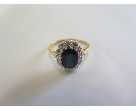 An 18ct gold sapphire and diamond ring, the central sapphire approx 8.5mm x 6.5mm x 3.5mm - surrounded by round cut diamonds,