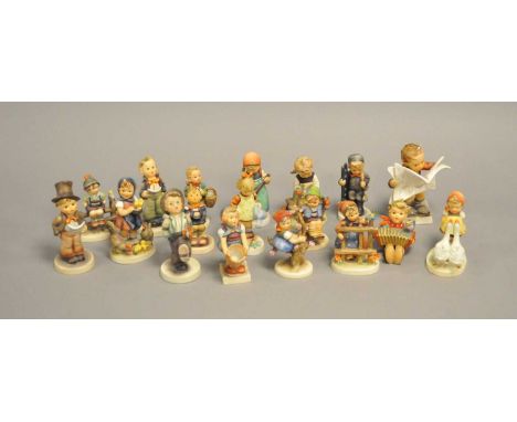 A group of Hummel figures, including a boy seated reading a newspaper, choirboys, boy on an apple tree, girl watering flowers