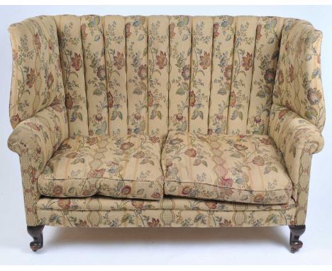 A Victorian wing back sofa, covered in a floral fabric, raised on claw and ball feet, 110 cm high, 145 cm wide, 60 cm deep.