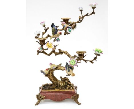 A bronzed metal and porcelain three light candelabra modelled as flowering bonsai trees with birds in the branches, on four f