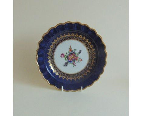 A Worcester wet blue plate painted with flowers inside an elaborate gilt border, circa 1768-1772, Frett mark, 19 cm diameter 