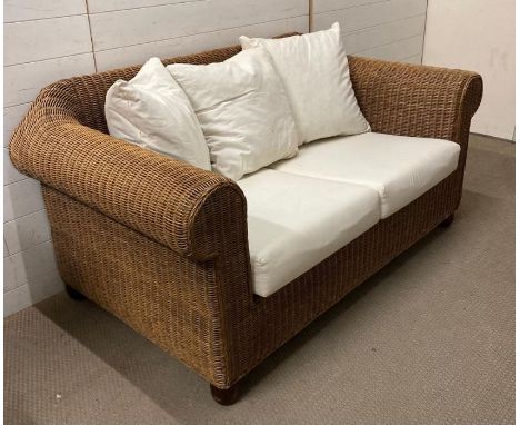 A two seater wicker sofa with white linen upholstered cushions 