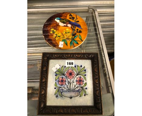 A CIRCULAR TILE DECORATED WITH A BIRD EATING FRUIT TOGETHER WITH A FRAMED FLORAL TILE
